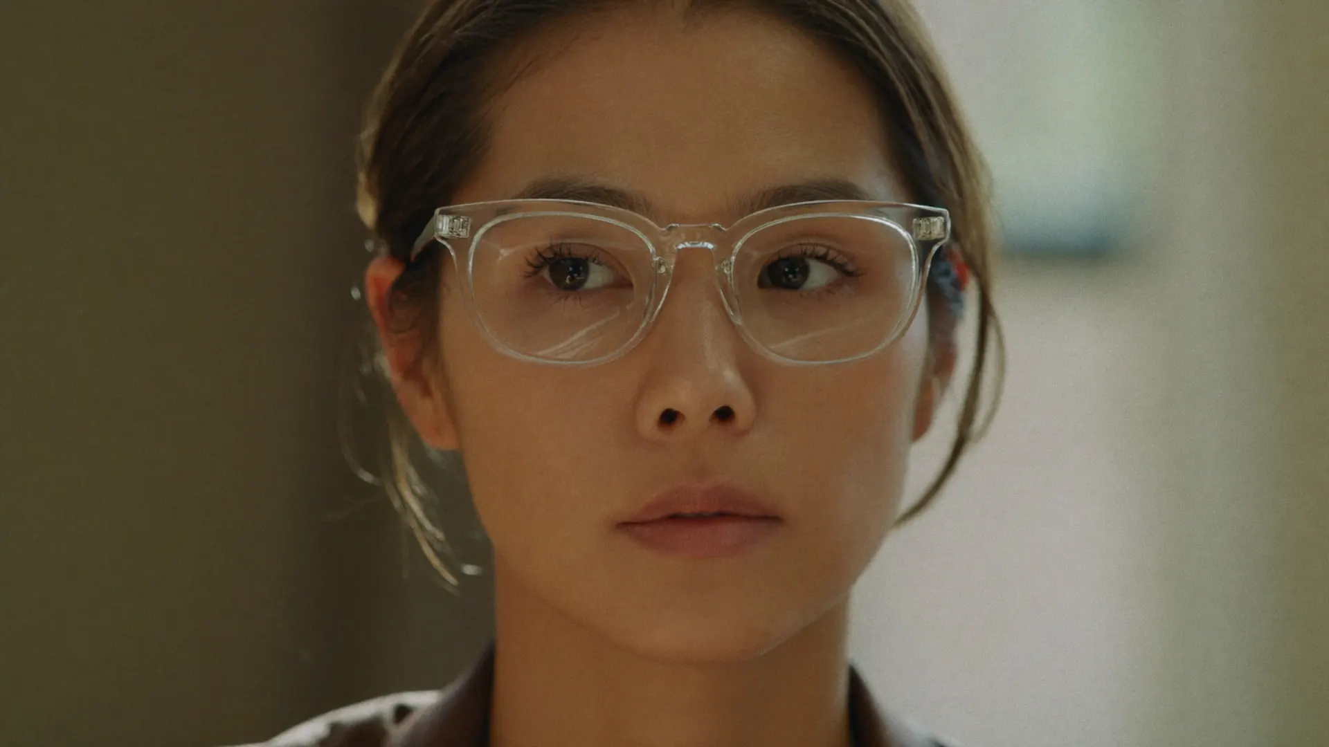 A woman indoors in clear eyeglasses — the photochromic lenses fully transparent, her eyes bright and visible.